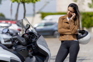 Woman with broken down motorcycle calling workshop tow truck