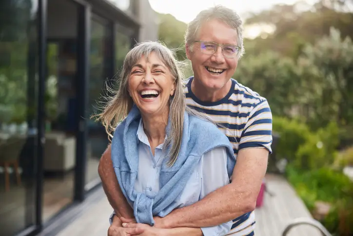 Mature couple standing arm in arm together and laughing outside of their home in Grand Junction, CO