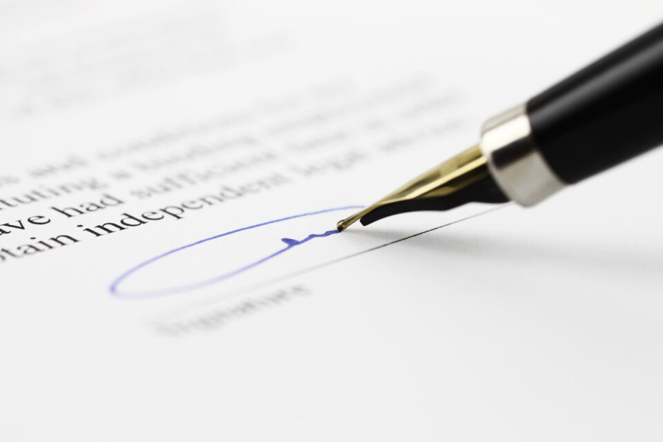Close-up of a fountain pen signing a document with blue ink on a signature line