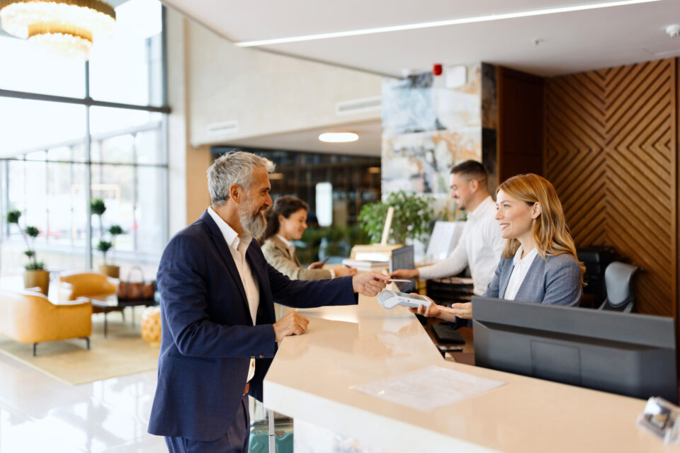 Male guest interacting with a female receptionist at a modern hotel reception desk, highlighting hotel insurance services for hospitality businesses