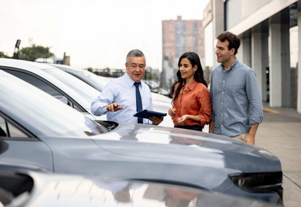 Agent discussing Auto Insurance options with couple near parked cars in Greater Phoenix Area.