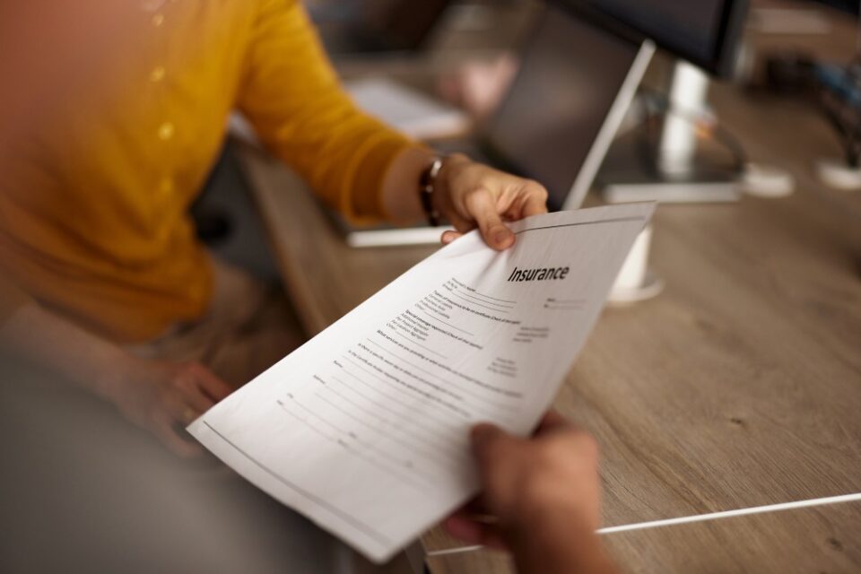 Person in a yellow sweater reviewing an insurance document across a desk in Glendale, AZ